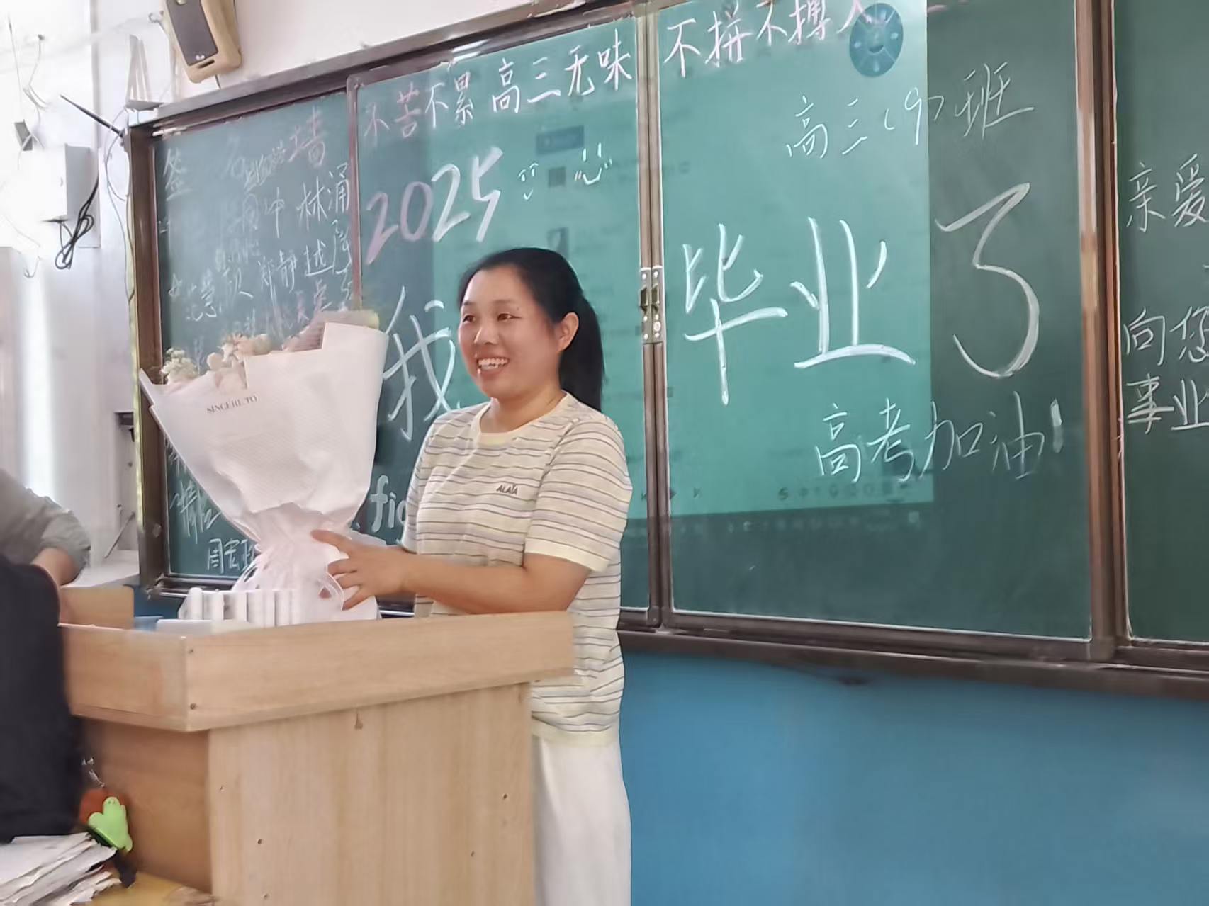 班主任抱着学生送的花束，在黑板前笑